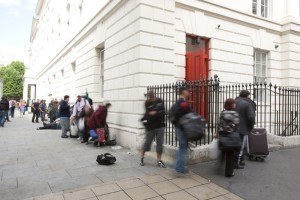 queue of people waiting to go in to white building with red door